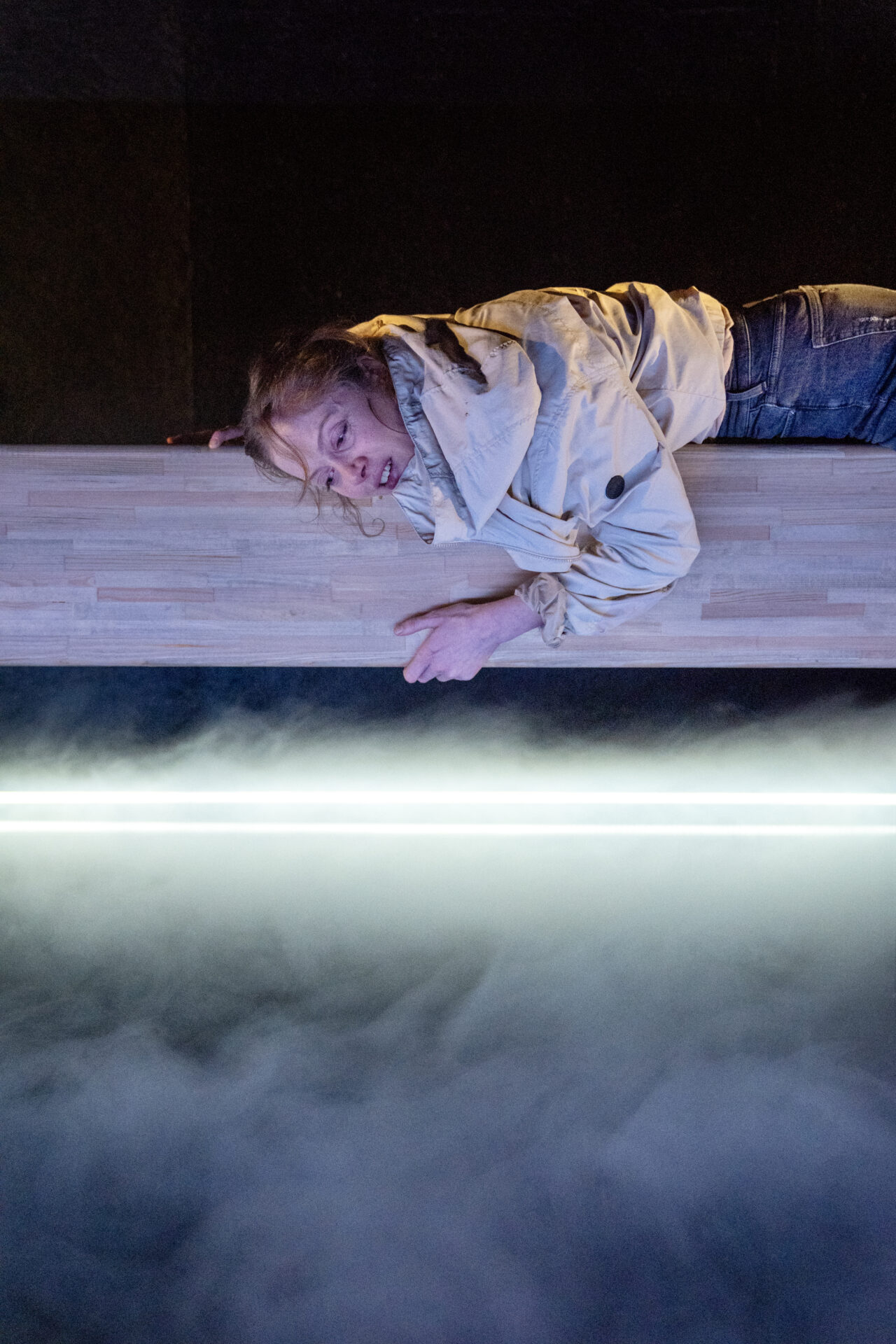 En kvinnelig skuespiller som ligger på scenekanten og titter ned - fra stykket Eg er vinden