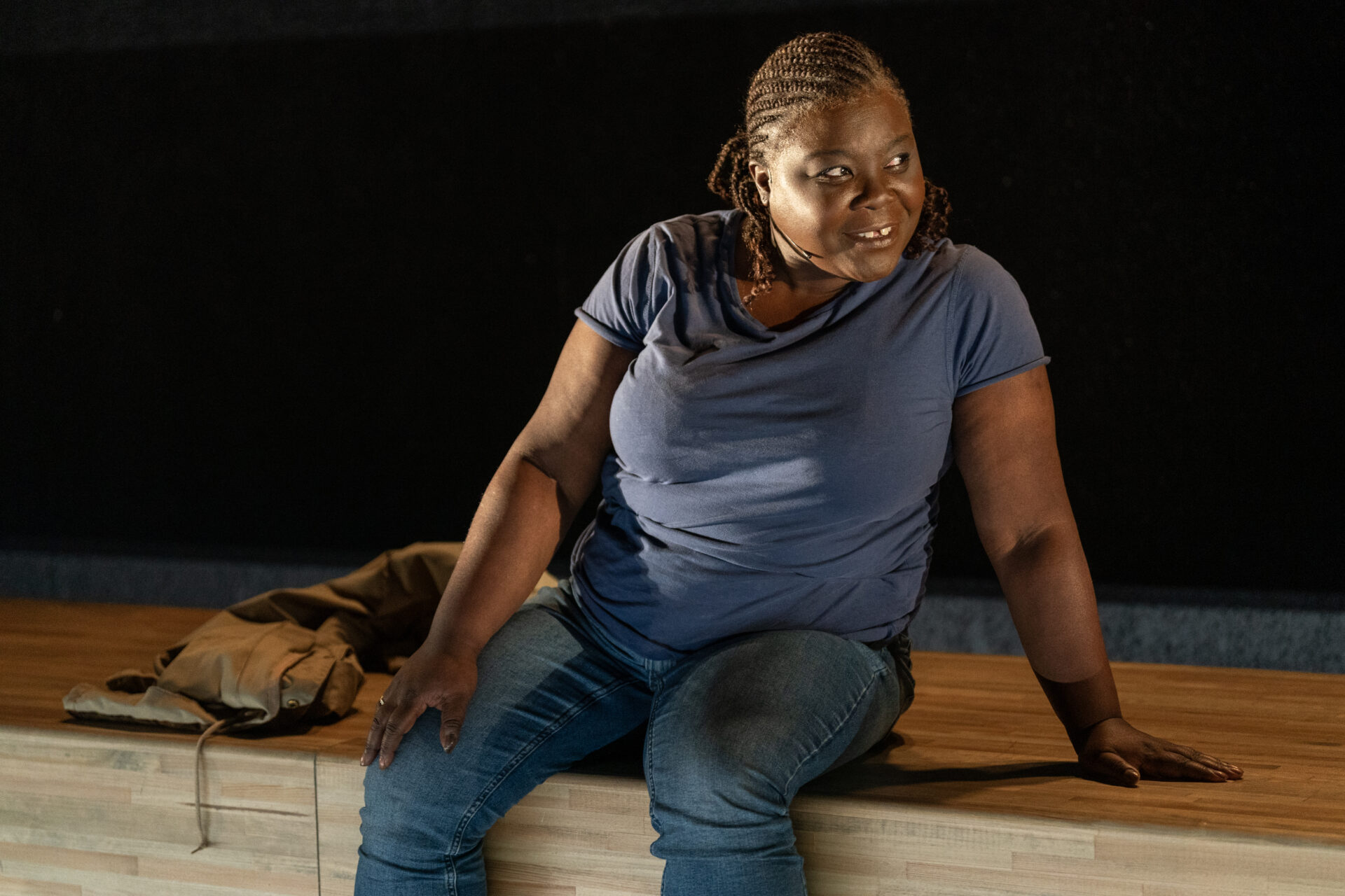 En skuespiller som sitter på scenekanten, ser til siden og smiler - fra stykket Eg er vinden