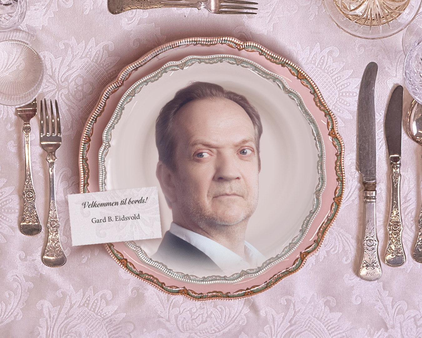 Nærbilde av et fint tildekket bord med portrett av en mann på tallerkenen. På et kort nær tallerkenen står det "Velkommen til bords! Gard B. Eidsvold."