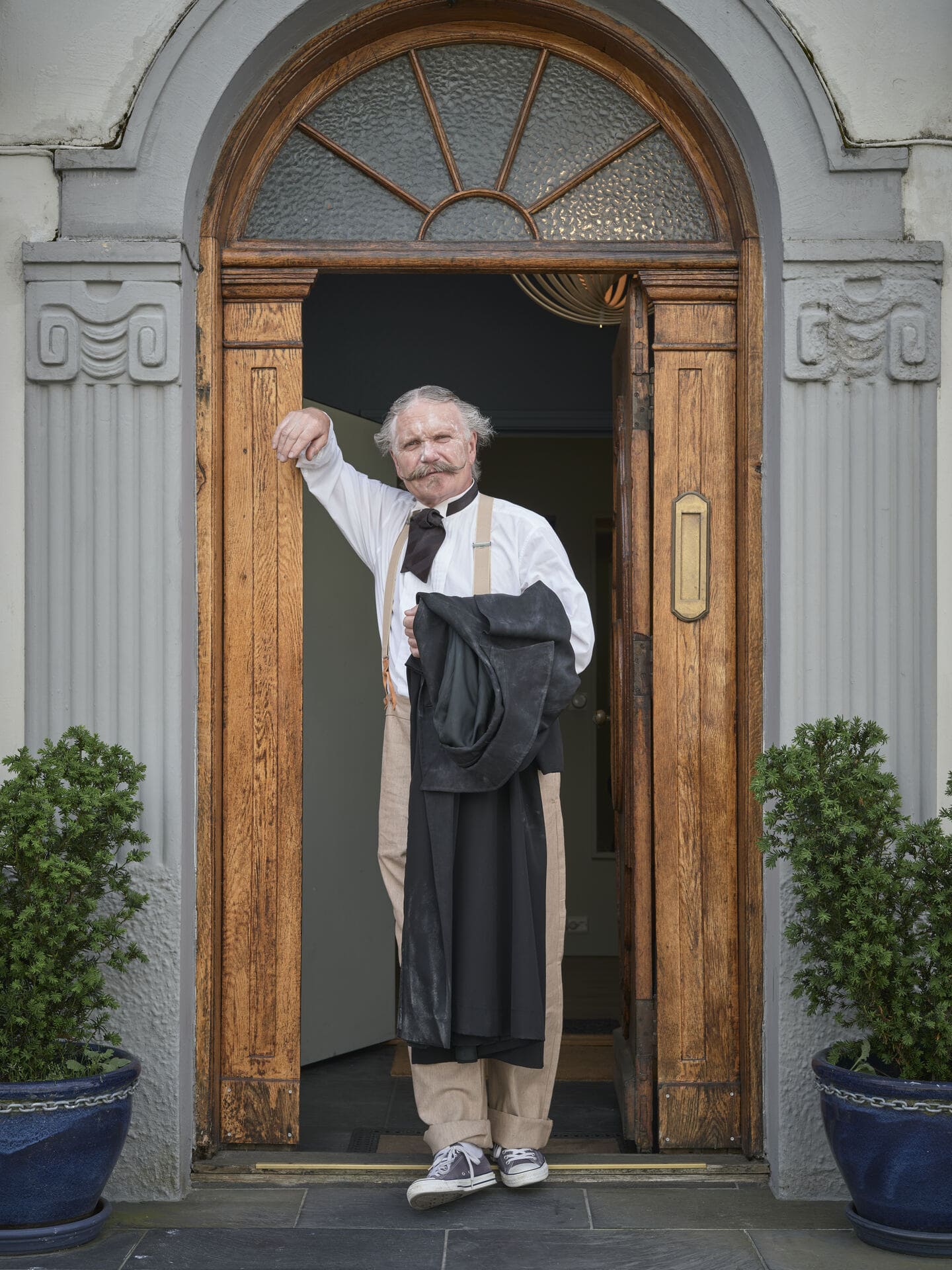 En mann i gammeldagse klær lener seg mot en dørkarm.