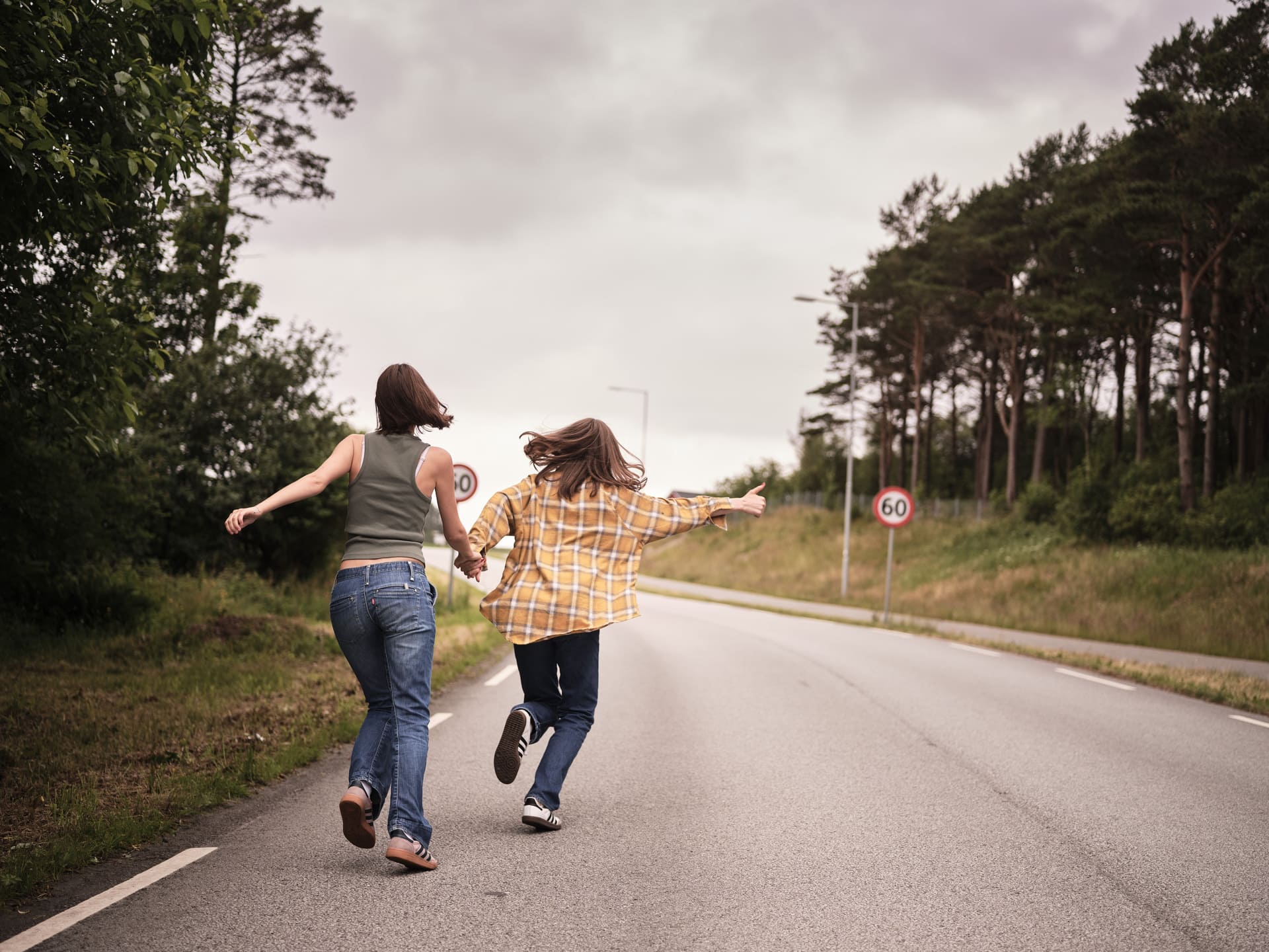 To ungdomsjenter løper side om side langs en landevei med ryggen til kamera.