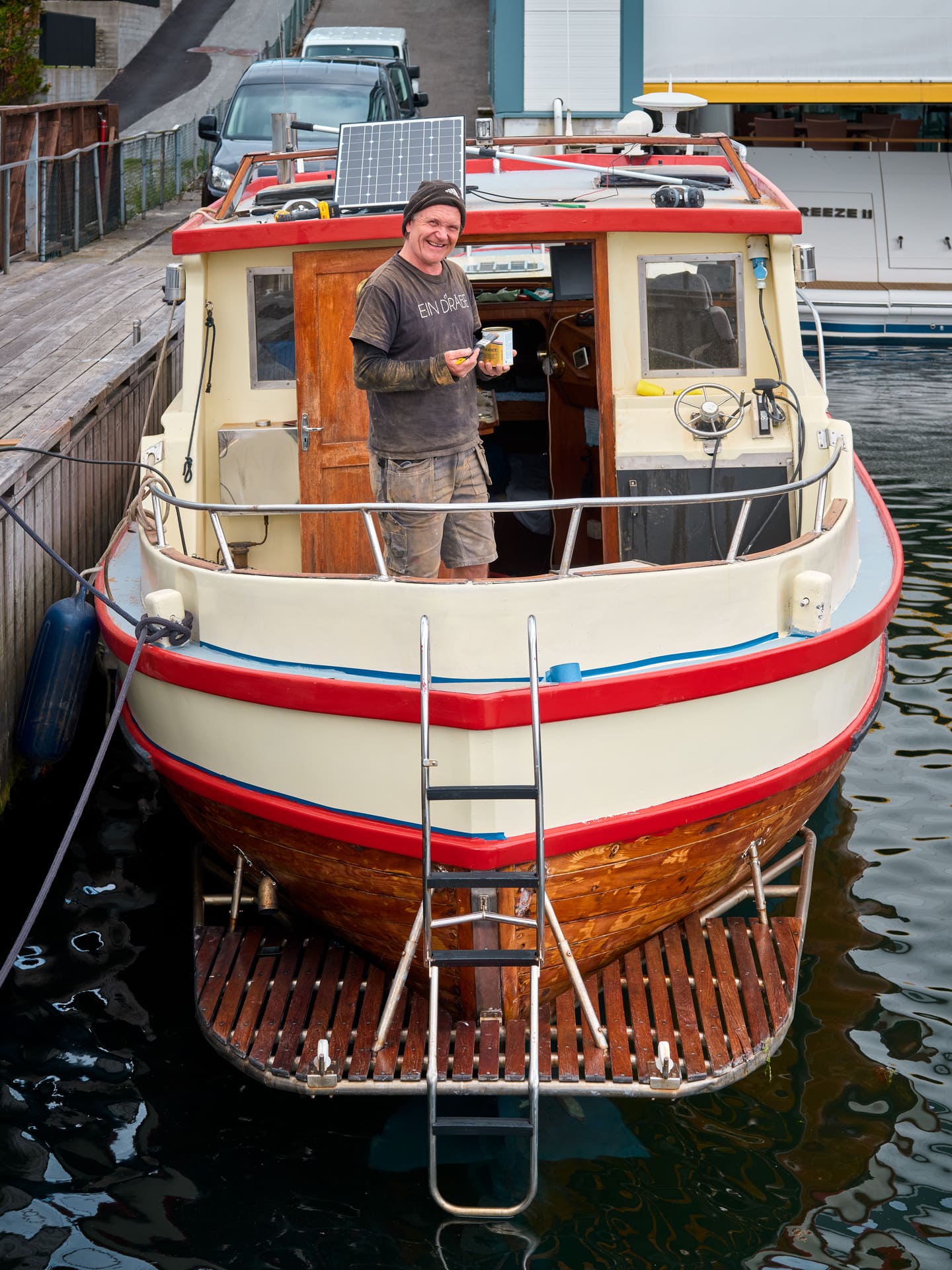 En smilende mann står i trebåt med maling og malerkost.