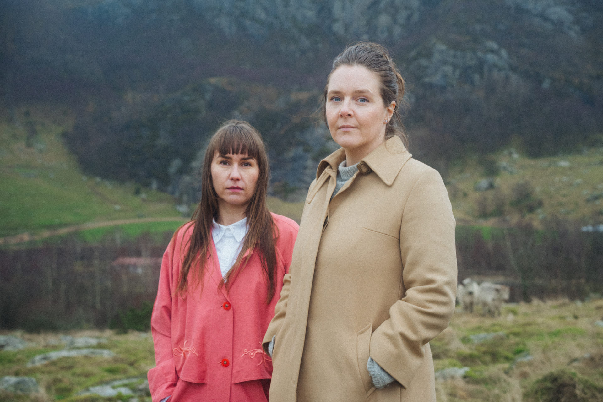 To kvinner ser inn i kamera. I bakgrunnen er det typisk norsk natur.