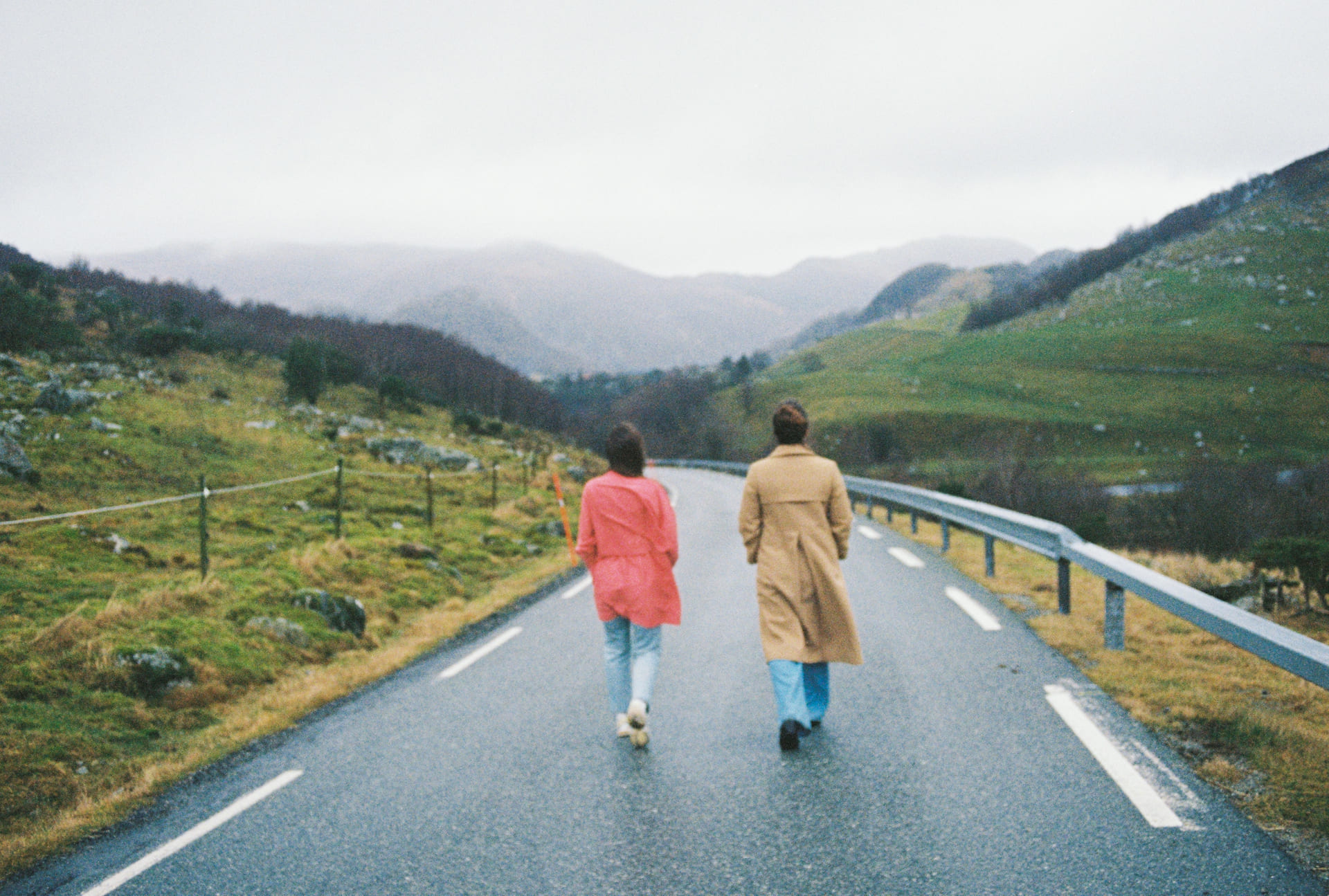 To kvinner går med ryggen mot kamera langs en landevei.