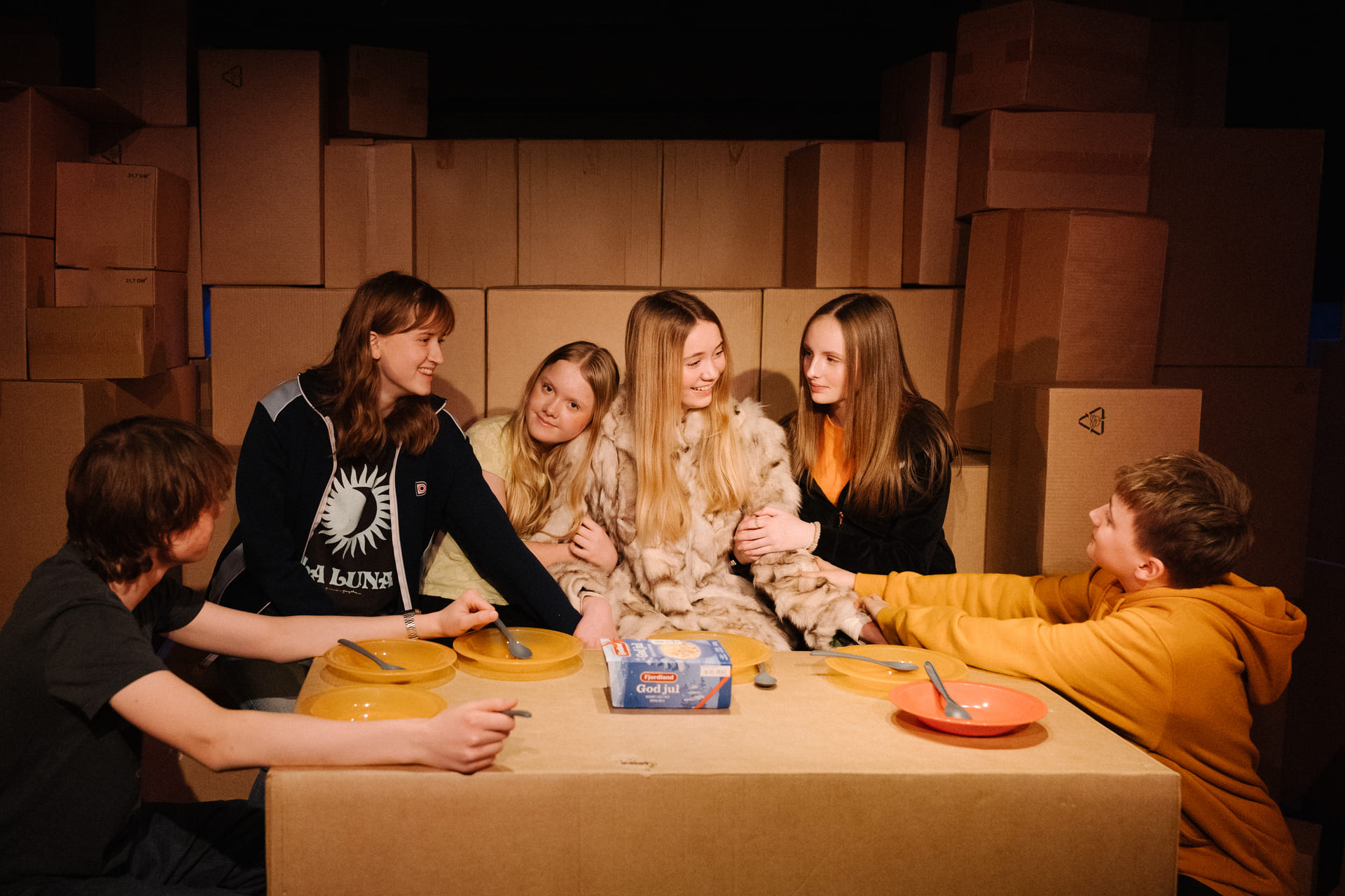 Seks ungdommer sitter rundt et bord, omringet av pappesker.