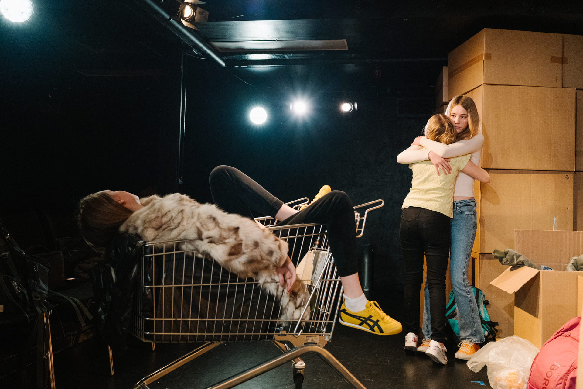 To jenter klemmer hverandre, mens en tredje ligger utstrakt i en handlevogn.