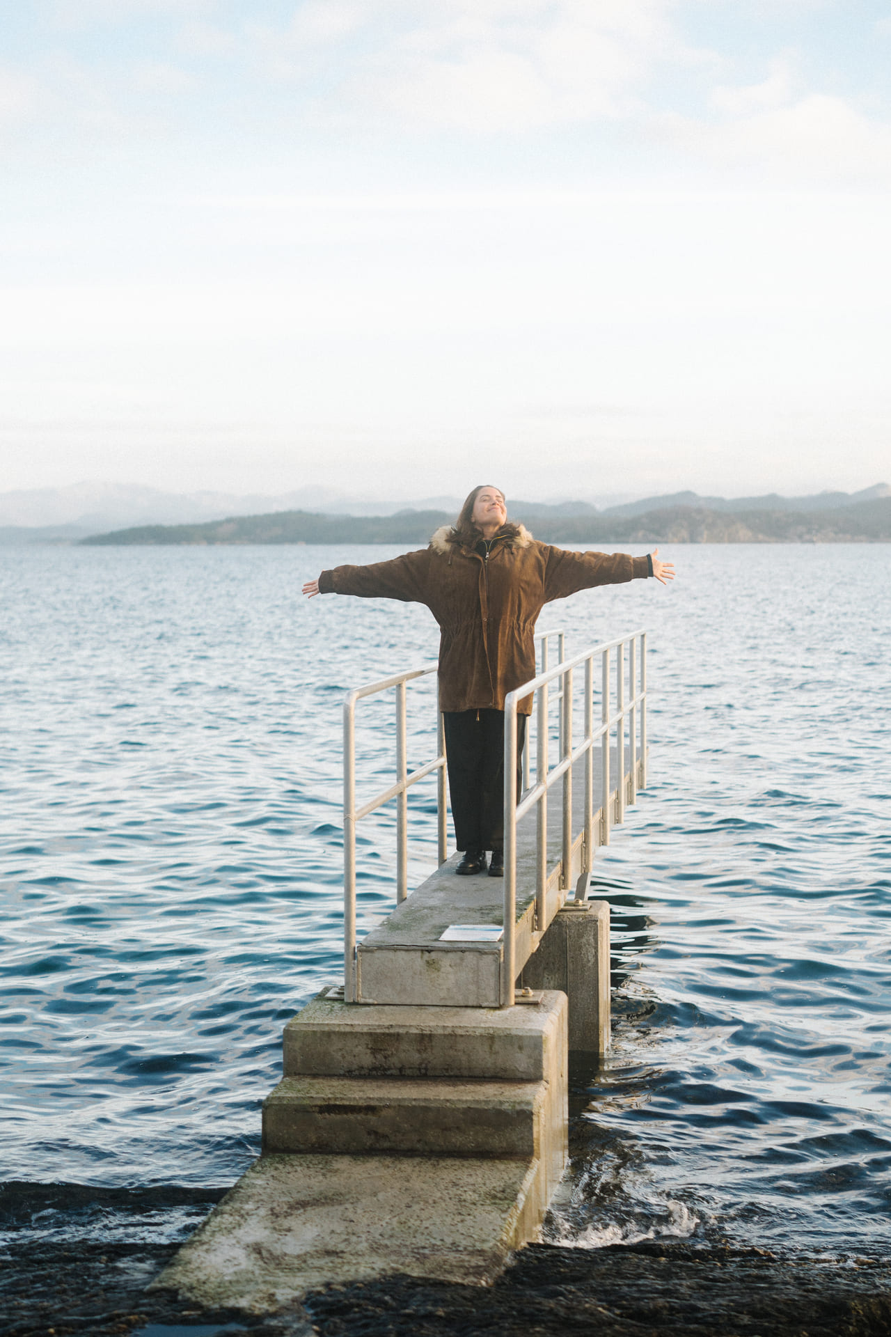 Kvinne står ved havet med armene utstrakt