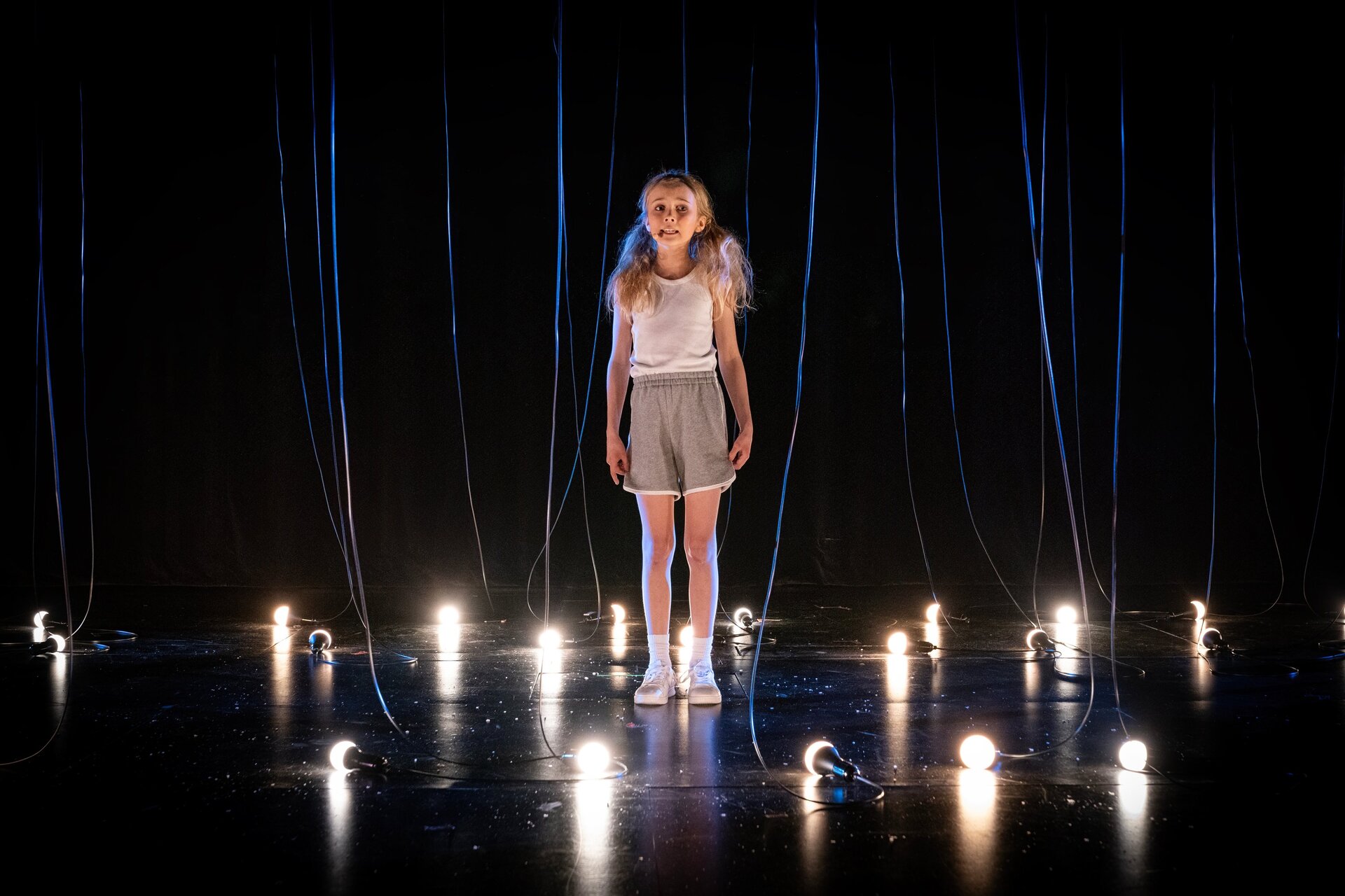 Jente står alene på en scene blant lys.