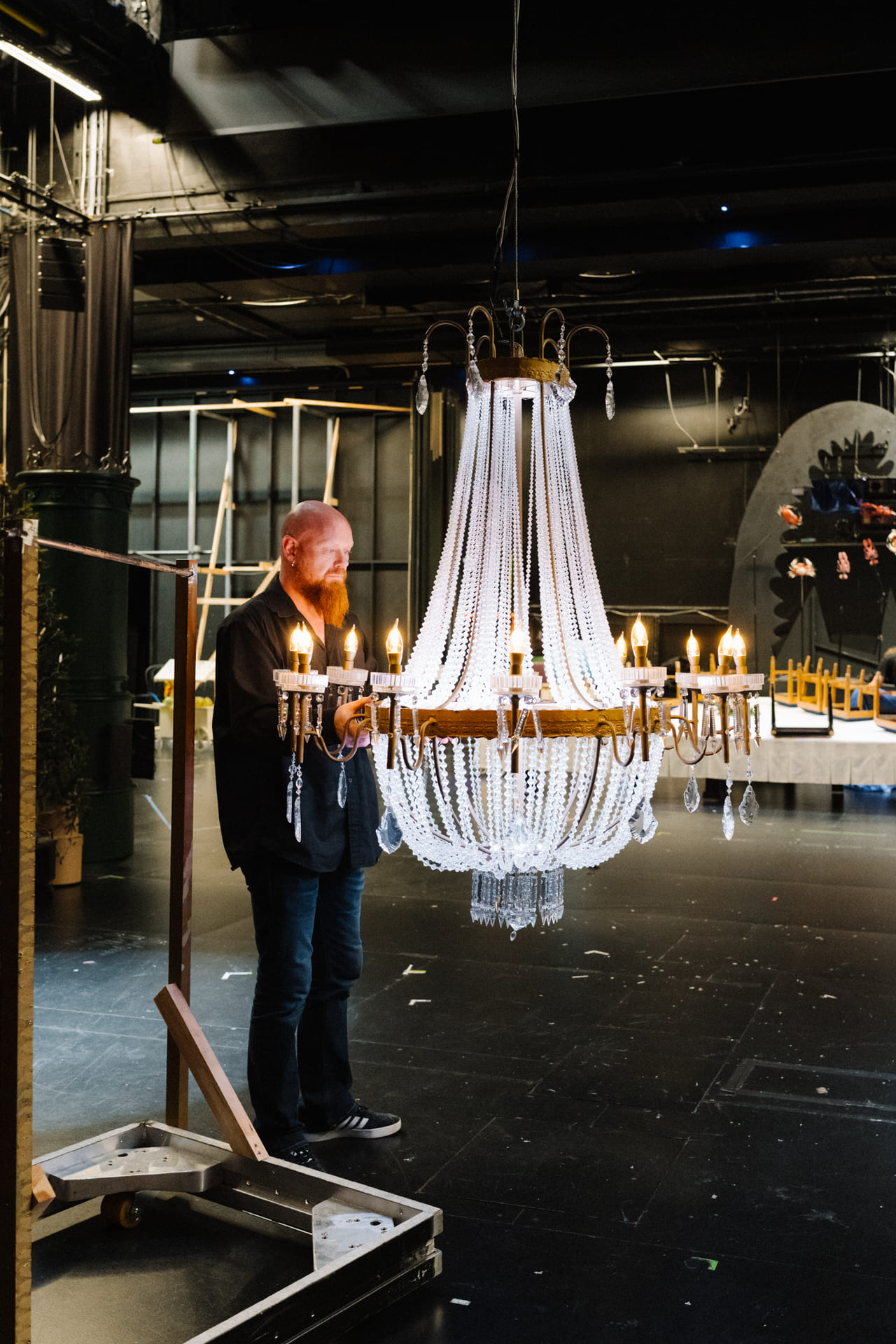 En mann står ved en stor lysekrone bak teaterscenen.