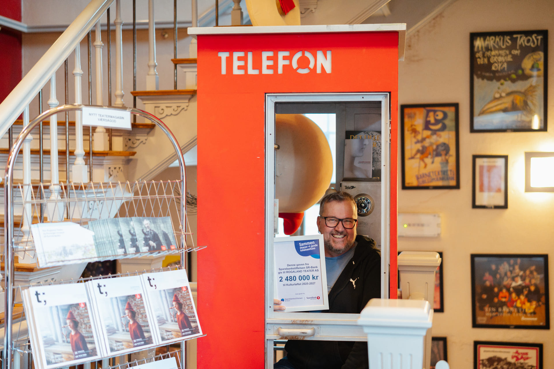 En mann står inni en retro telefonkiosk inne i teaterfoajeen.