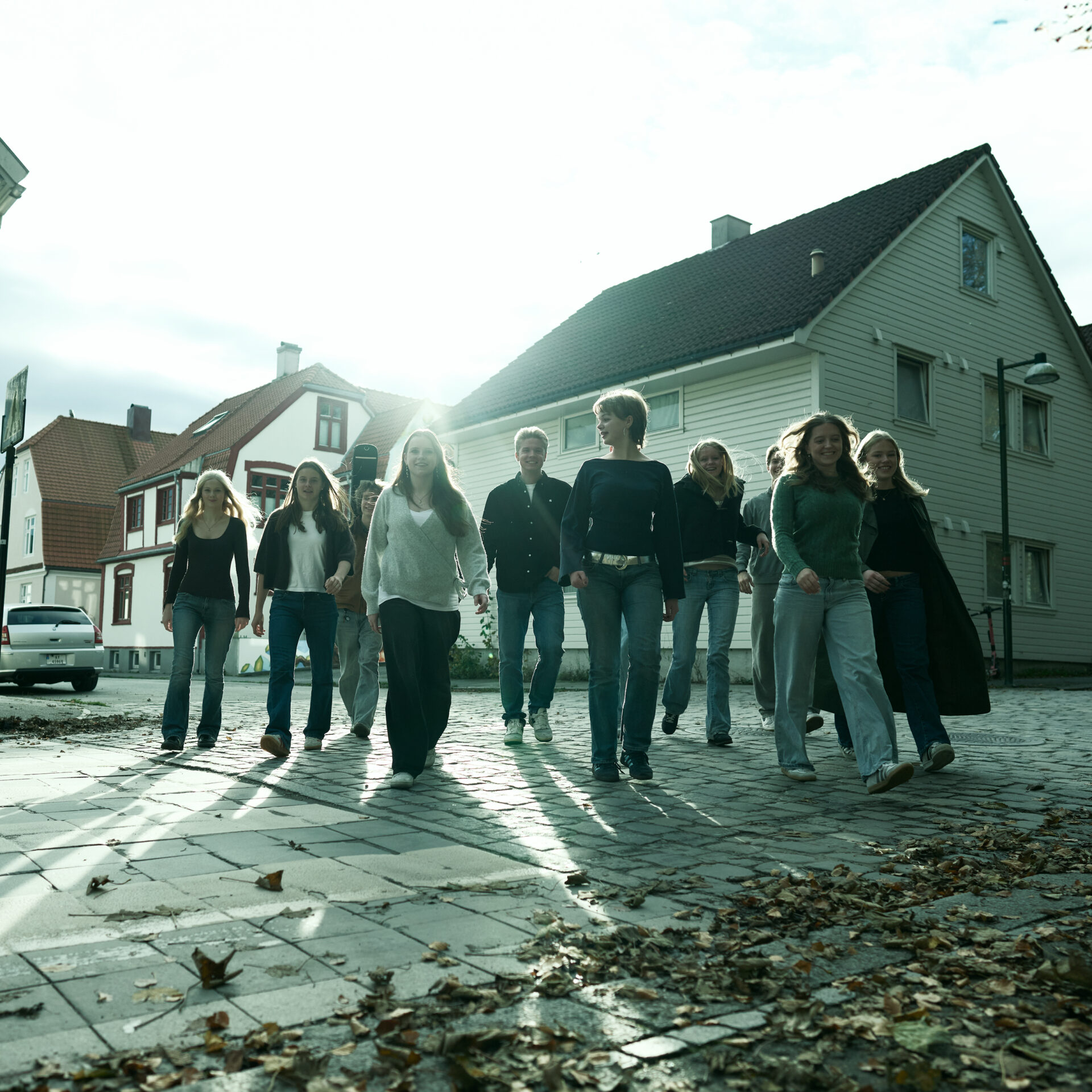 En gruppe ungdommer går mot kamera. De er i en brosteinsgate blant hvite hus.