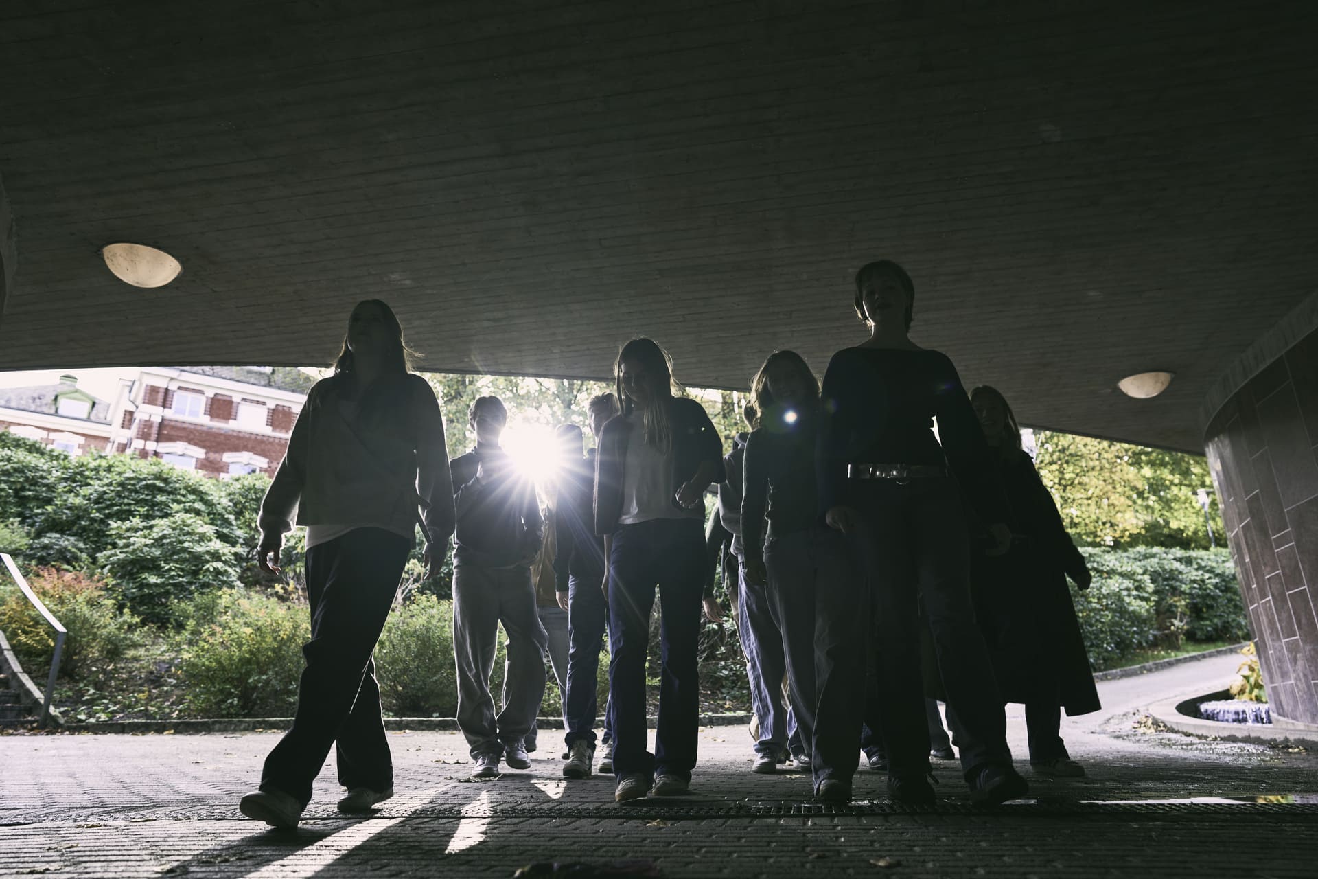 En gruppe ungdommer står i skygge under et utvendig tak.